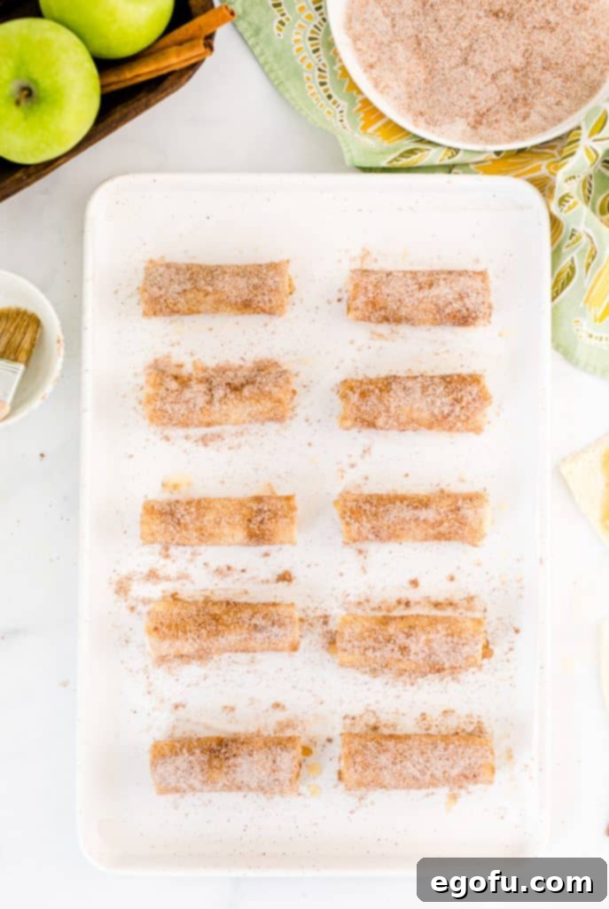 A buttered bread rollup being rolled in the combined sugar, cinnamon, and nutmeg mixture, ensuring a complete and even coating.