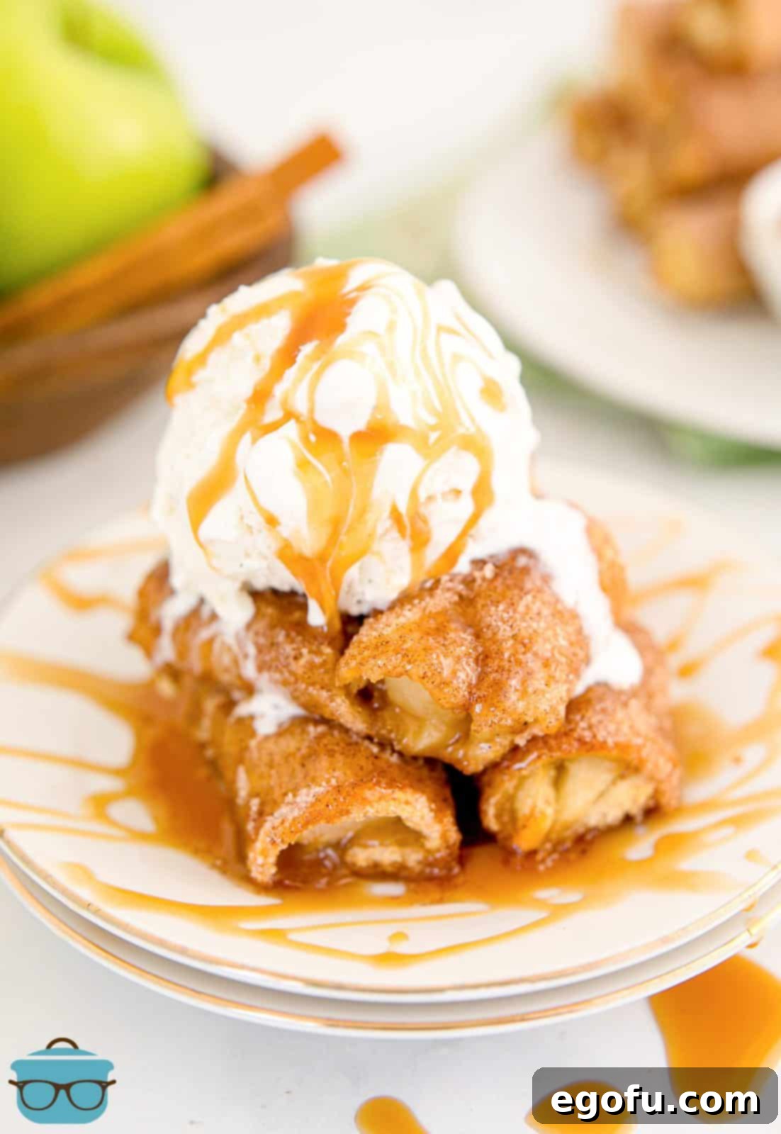 A mouthwatering stack of Baked Apple Pie Rollups, generously topped with a scoop of creamy vanilla ice cream and rich caramel sauce, ready to be enjoyed.