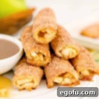Close-up square image of stacked Baked Apple Pie Rollups next to a dish of rich caramel sauce.