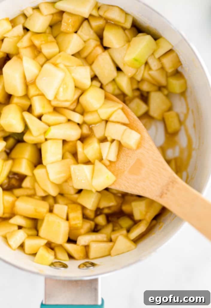 Diced apples stirred into the simmering caramel-brown sugar sauce within a white saucepan, softening gently.