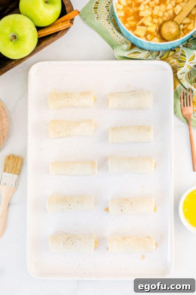 A slice of bread perfectly rolled up around the apple filling, showing a neat cylinder ready for coating and baking.