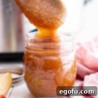 Square image of Apple Butter being placed in jar with wooden spoon.