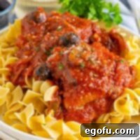 Square image of finished Chicken Cacciatore over noodles on white plate.