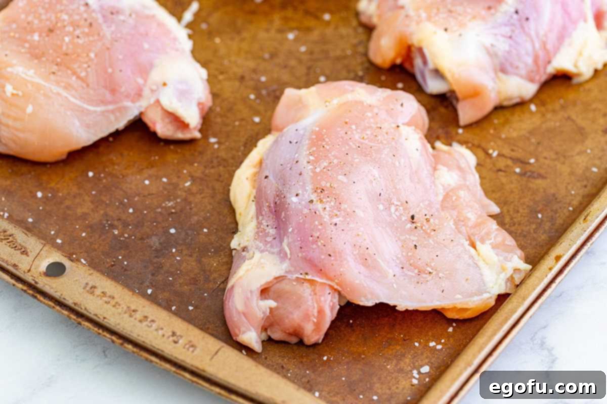 Chicken thighs on pan covered with salt and pepper, ready for flour.