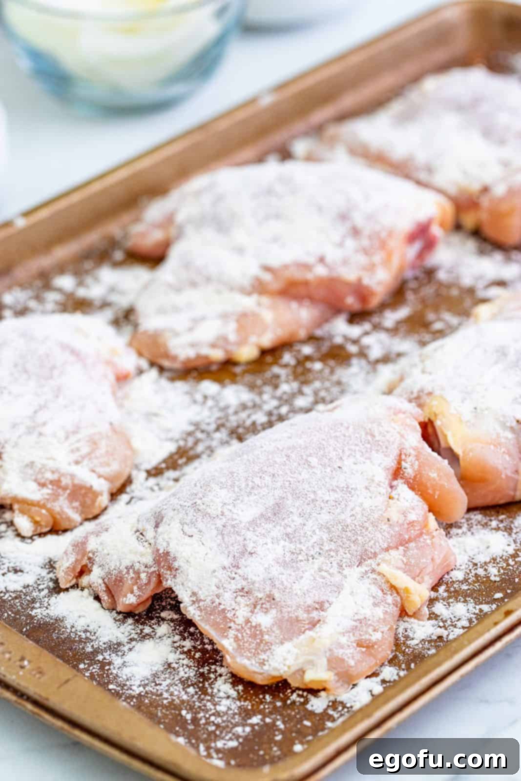 Flour coating chicken thighs on pan, ready for searing.
