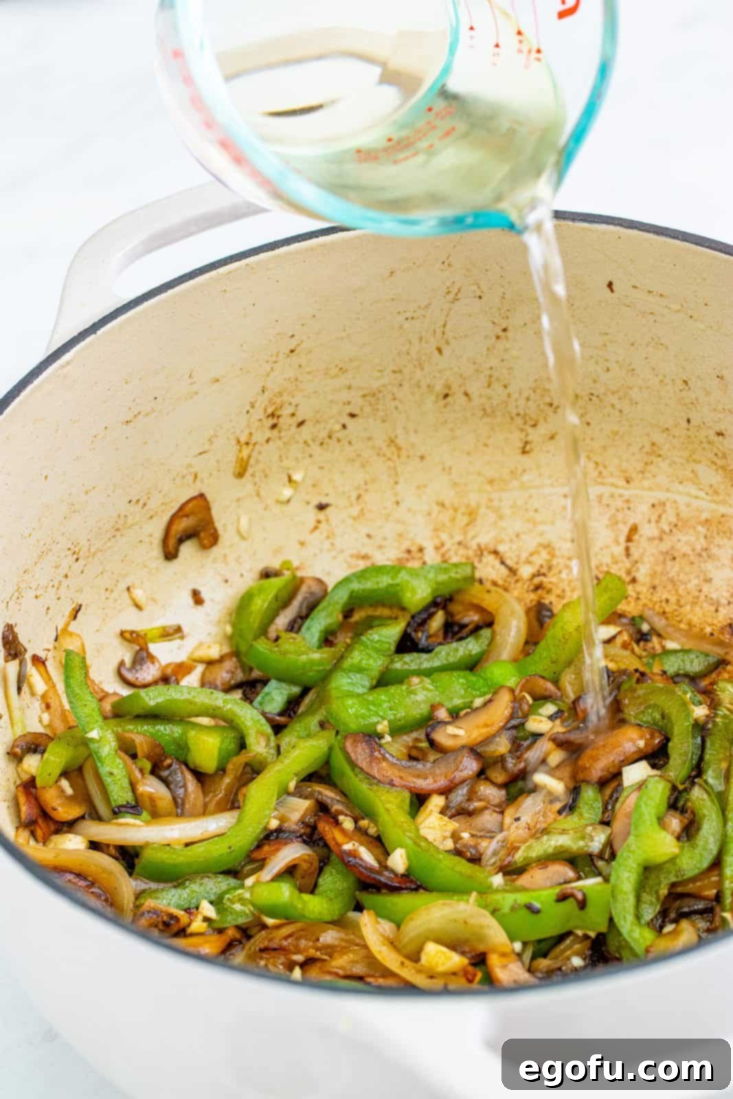 White wine being poured into the Dutch oven to deglaze the pan, scraping up browned bits.