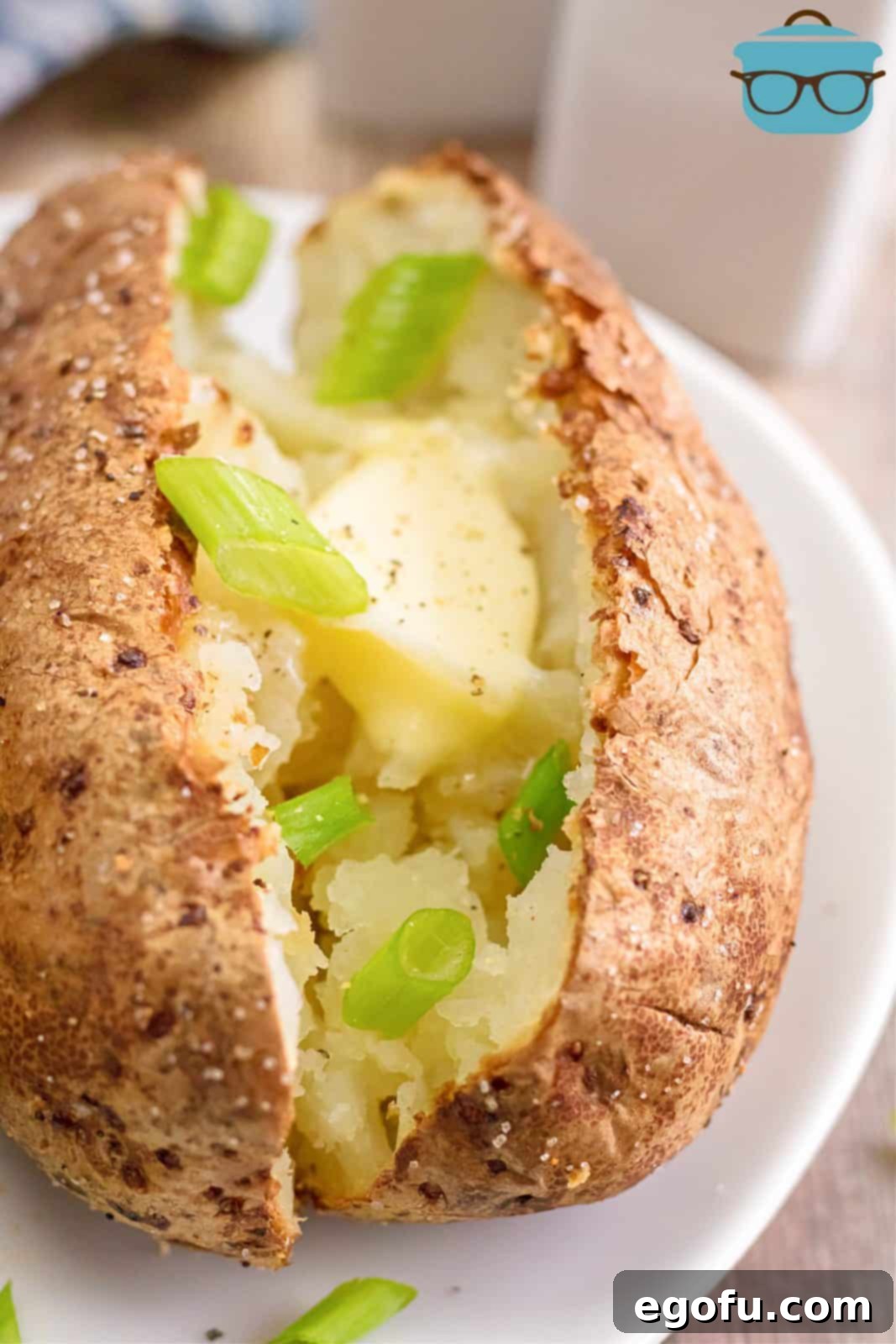 Close up of Air Fryer Baked Potato with butter and green onion on white plate.