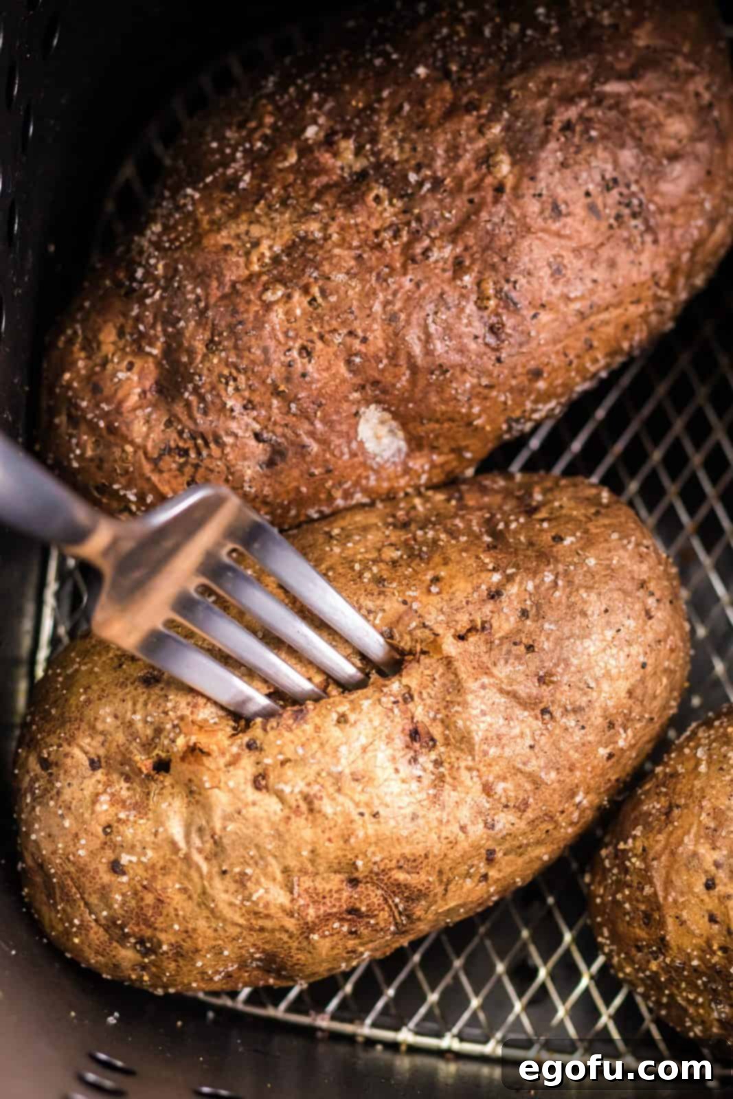 Finished potatoes in air fryer being poked with fork.