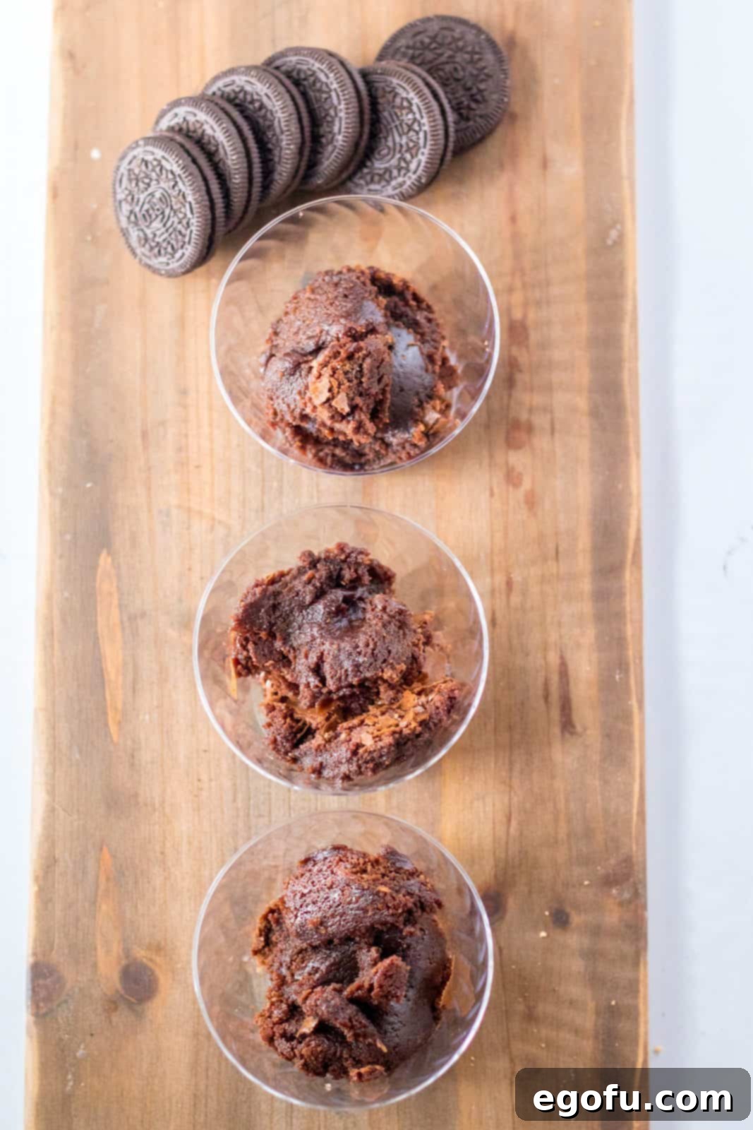 Brownies added to the bottom of clear plastic cups on a wooden board, ready for the next layer.
