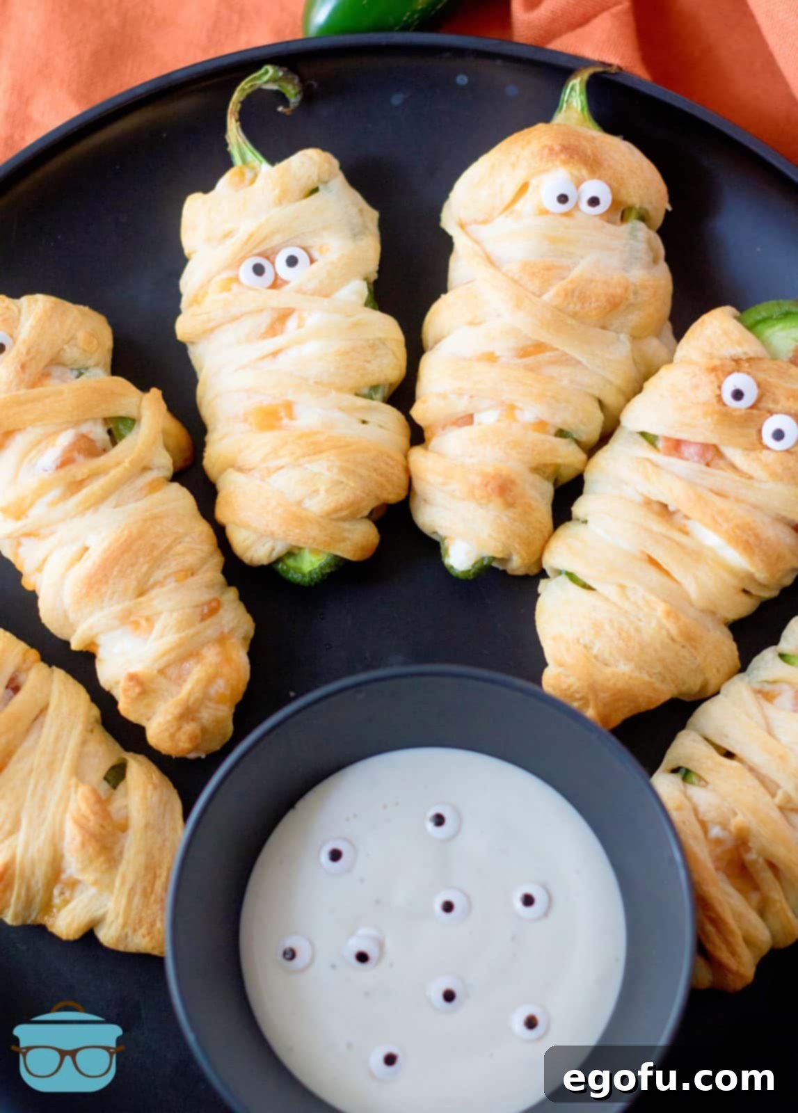 Mummy-Wrapped Jalapeño Poppers 2 Halloween Mummy Jalapeno Poppers on black plate with dipping sauce.