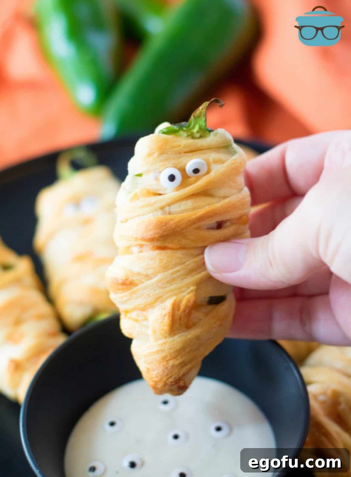 Mummy-Wrapped Jalapeño Poppers 7 Hand holding up one Halloween Mummy Jalapeno Popper showing off eyes.