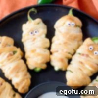 Mummy-Wrapped Jalapeño Poppers 9 Square image close up of Halloween Mummy Jalapeno Poppers on black plate.