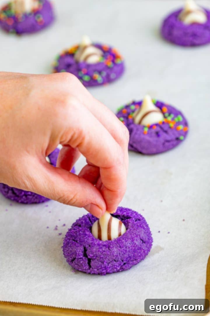 Baked cookies with a hand pressing a Hershey's Hug into the top of a warm cookie, forming the witch hat.