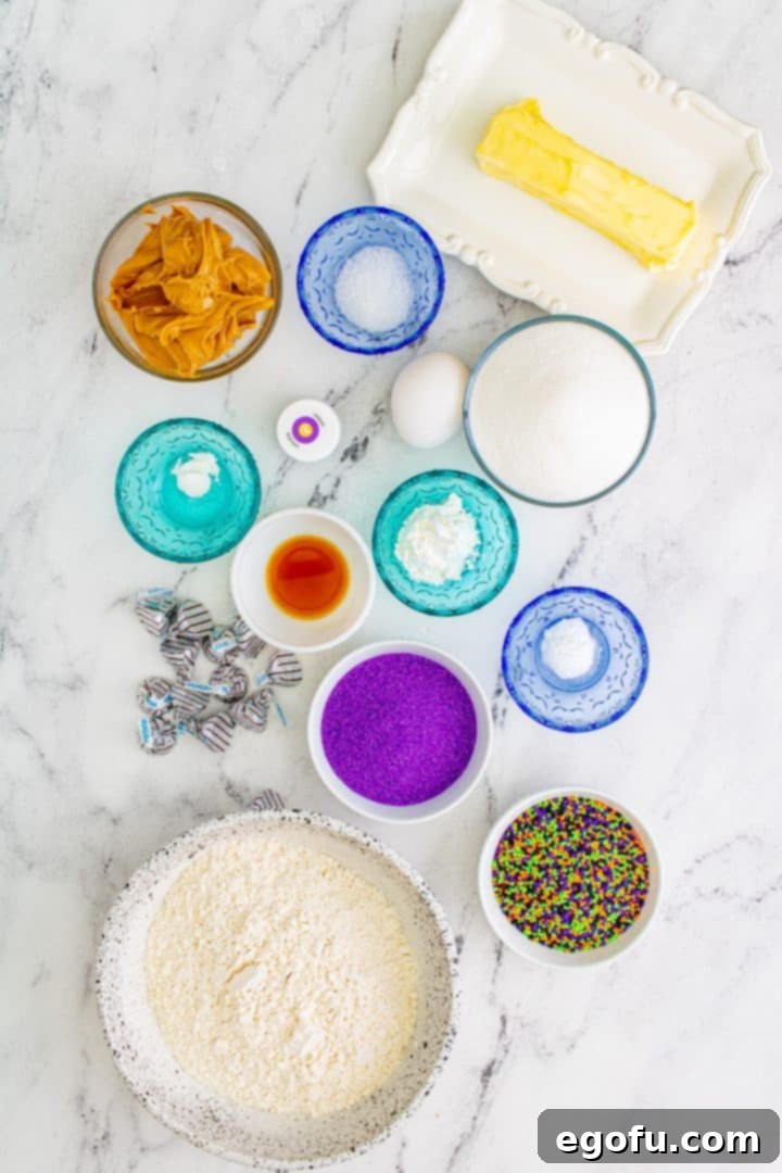 Ingredients needed: all-purpose flour, cornstarch, baking soda, baking powder, salt, butter, granulated sugar, egg, peanut butter, vanilla extract, purple gel food coloring, Halloween sprinkles or purple sanding sugar and hugs candies or chocolate kisses, arranged for baking.