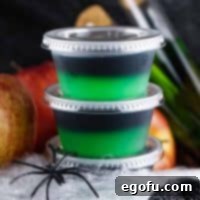 Square image of two stacked Halloween Poison Apple Jell-O Shots with fake spider and web.