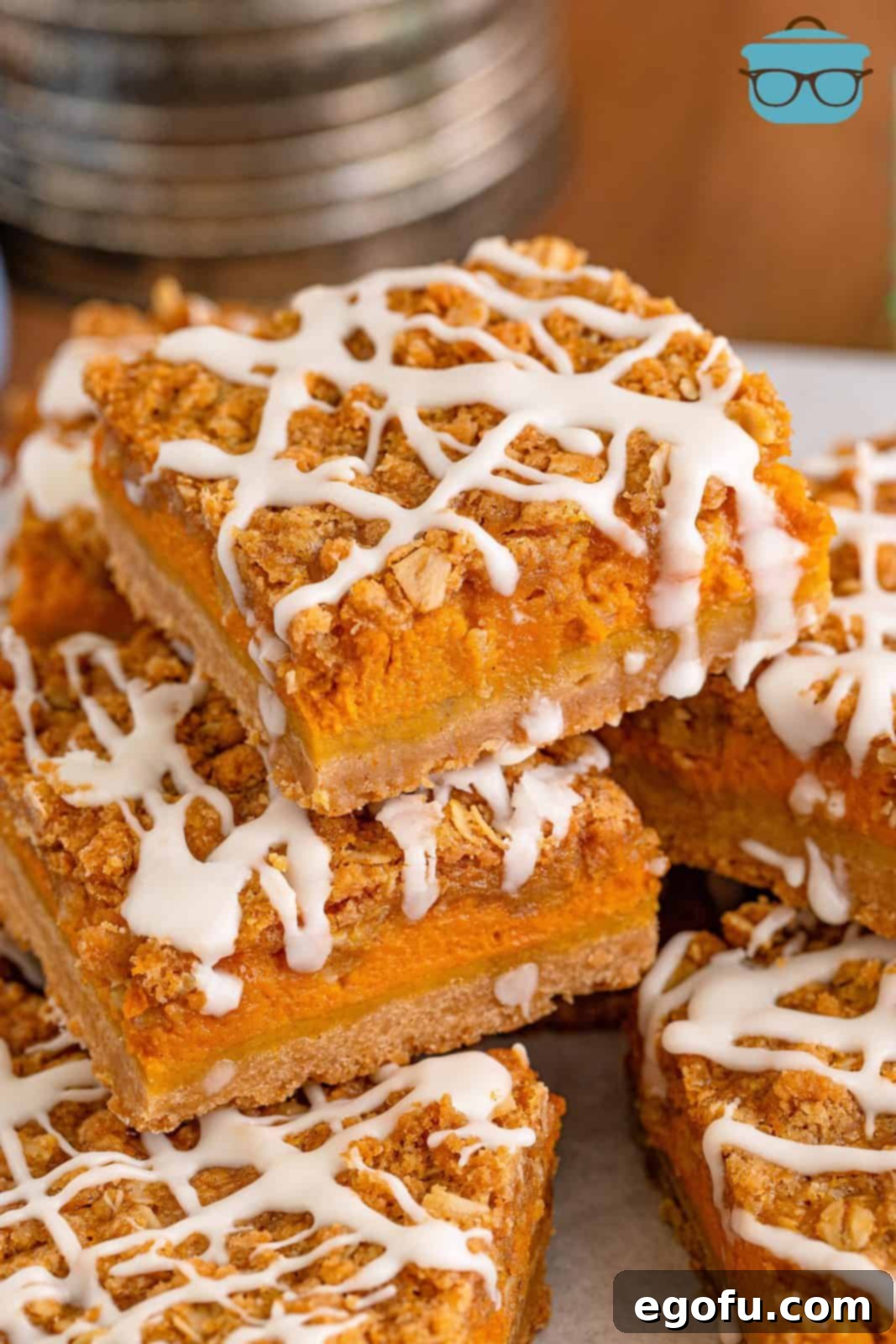 Close-up photo of a stack of pumpkin streusel bars on white parchment paper, showcasing the three distinct layers.
