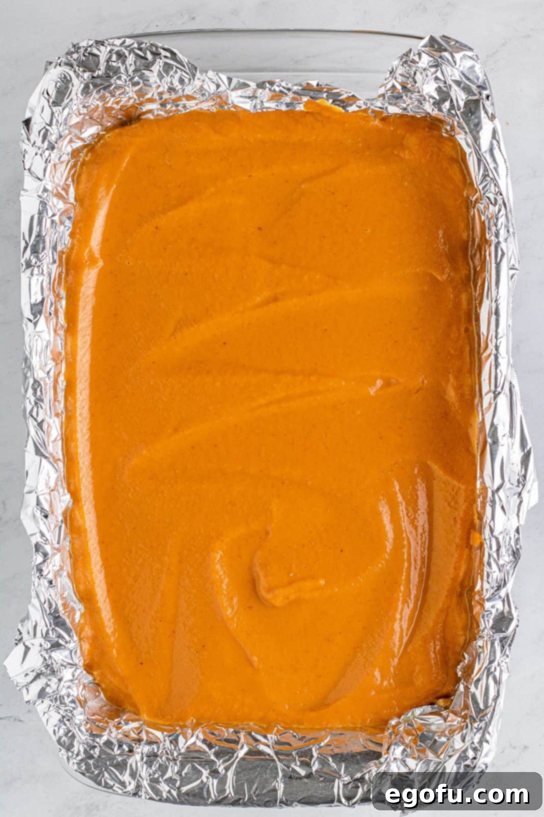 The smooth pumpkin filling is carefully poured over the baked crust in the baking pan.