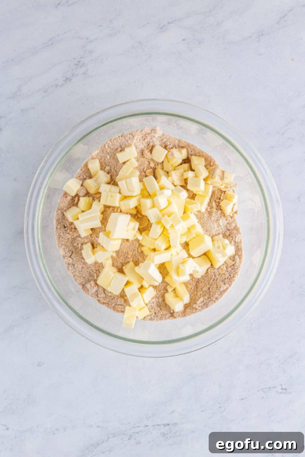 Cold butter is added to the dry streusel mixture in a clear bowl, ready to be cut in.