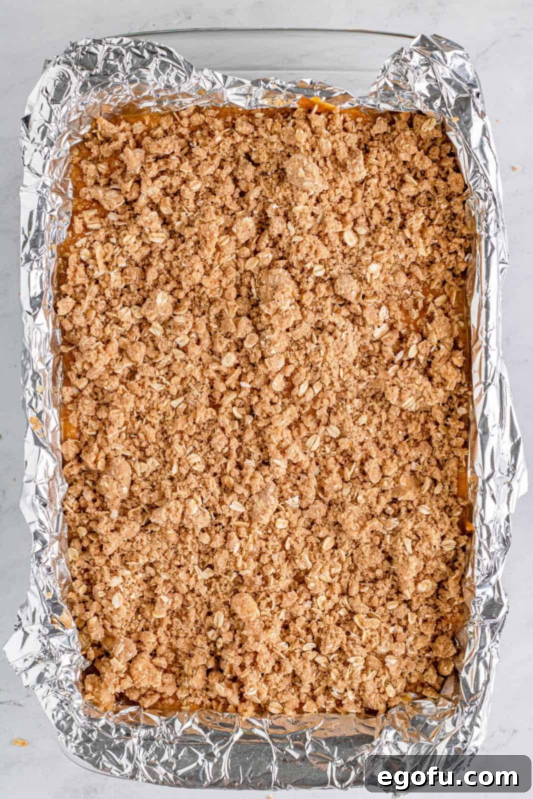 The crumbly streusel mixture is evenly sprinkled on top of the pumpkin filling in the baking pan.
