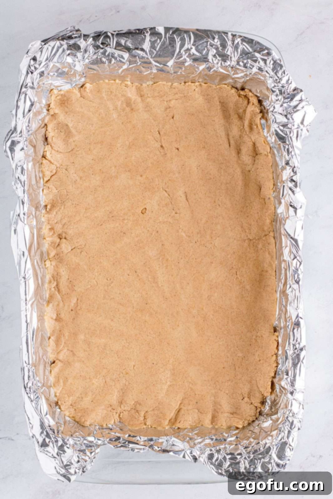 The crust mixture is pressed evenly into the foil-lined baking pan, ready for baking.