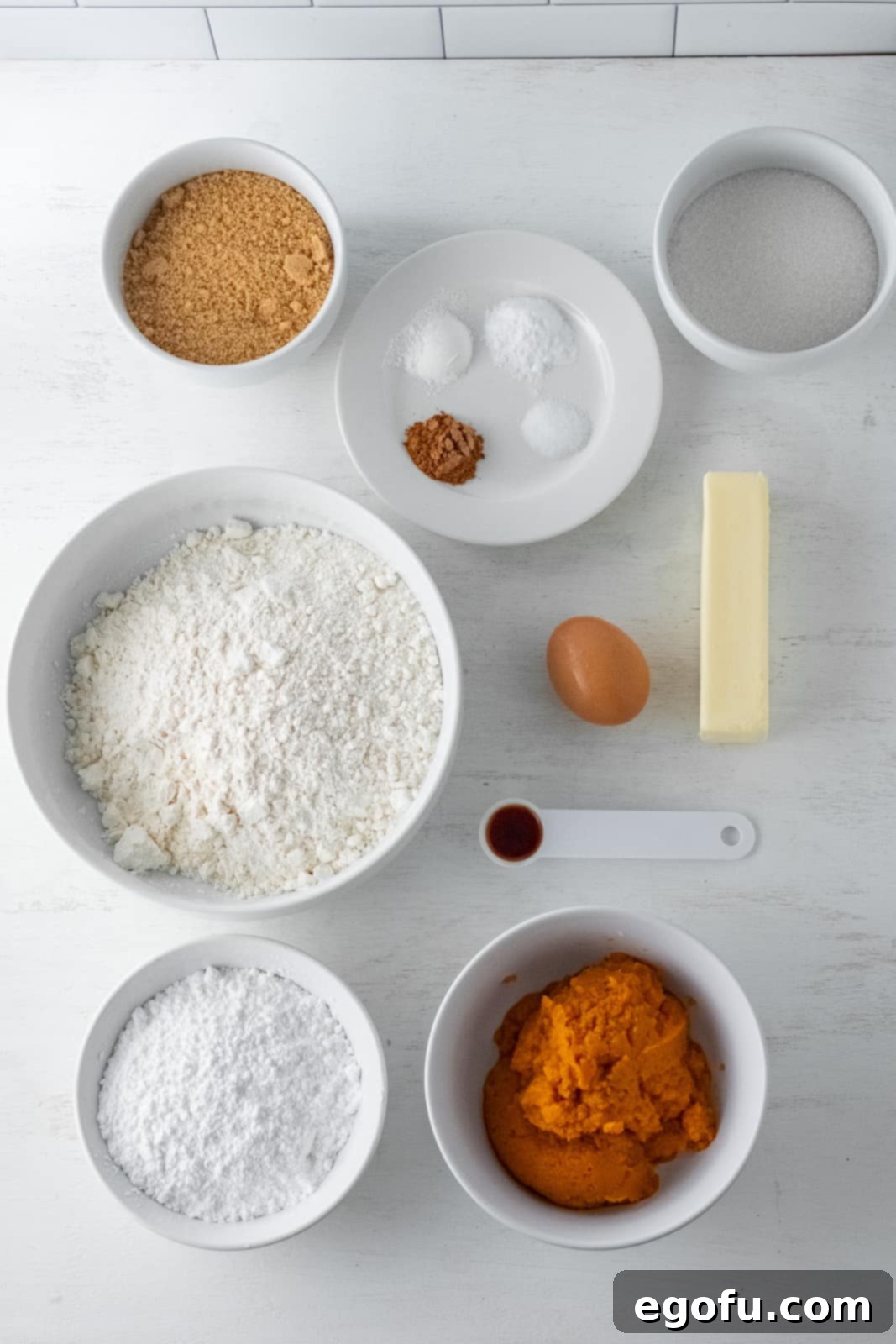 Fall Pumpkin Crinkle Delights 4 A vibrant display of all the ingredients needed: all-purpose flour, pumpkin pie spice, baking powder, baking soda, salt, softened butter, brown sugar, granulated sugar, a fresh egg, rich pumpkin puree, pure vanilla extract, and a generous bowl of powdered sugar.