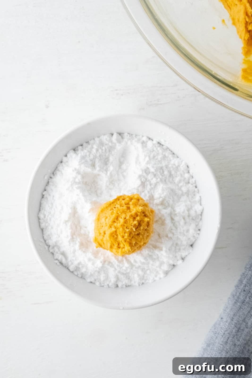 Fall Pumpkin Crinkle Delights 8 A perfectly scooped cookie dough ball dropped into a bowl generously filled with powdered sugar.