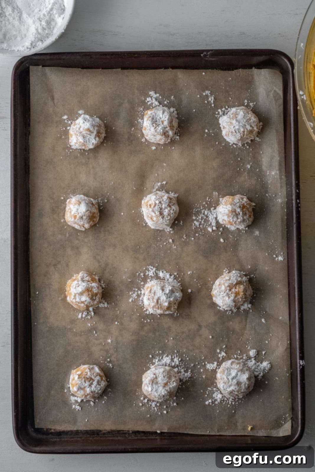 Fall Pumpkin Crinkle Delights 10 Evenly spaced cookie dough balls, heavily coated in powdered sugar, arranged on a lined baking sheet.