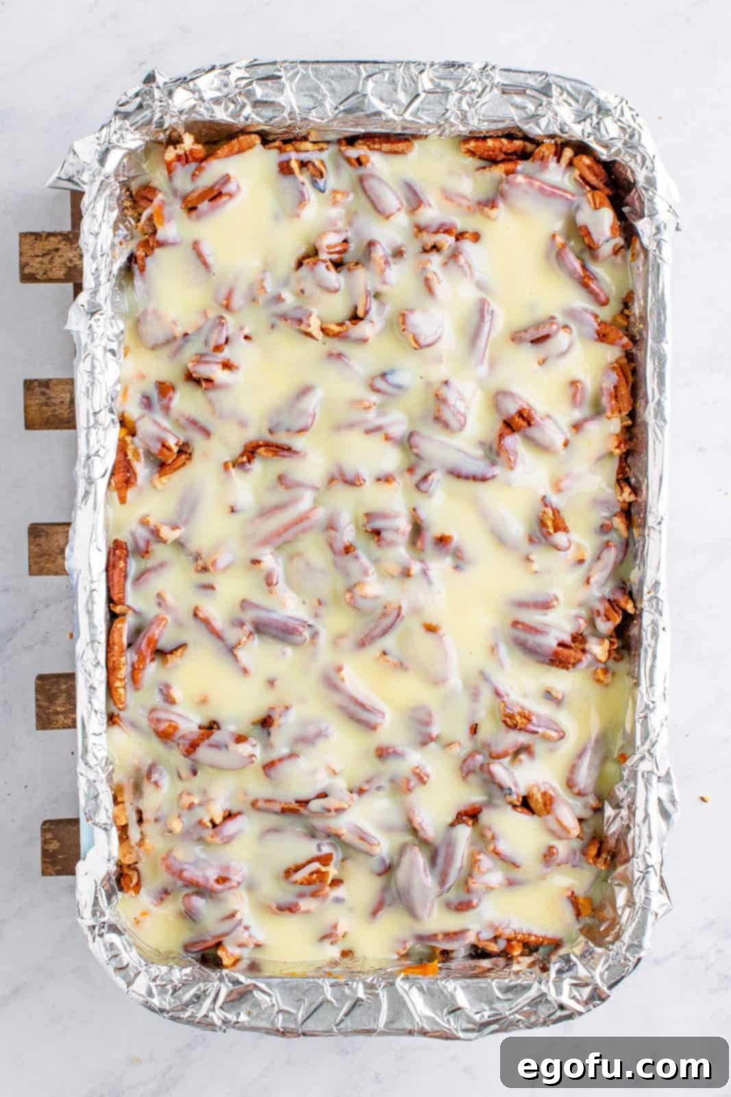 Autumn Magic Pumpkin Bars 10 Sweetened condensed milk being poured evenly over the layers of toppings in the baking pan.