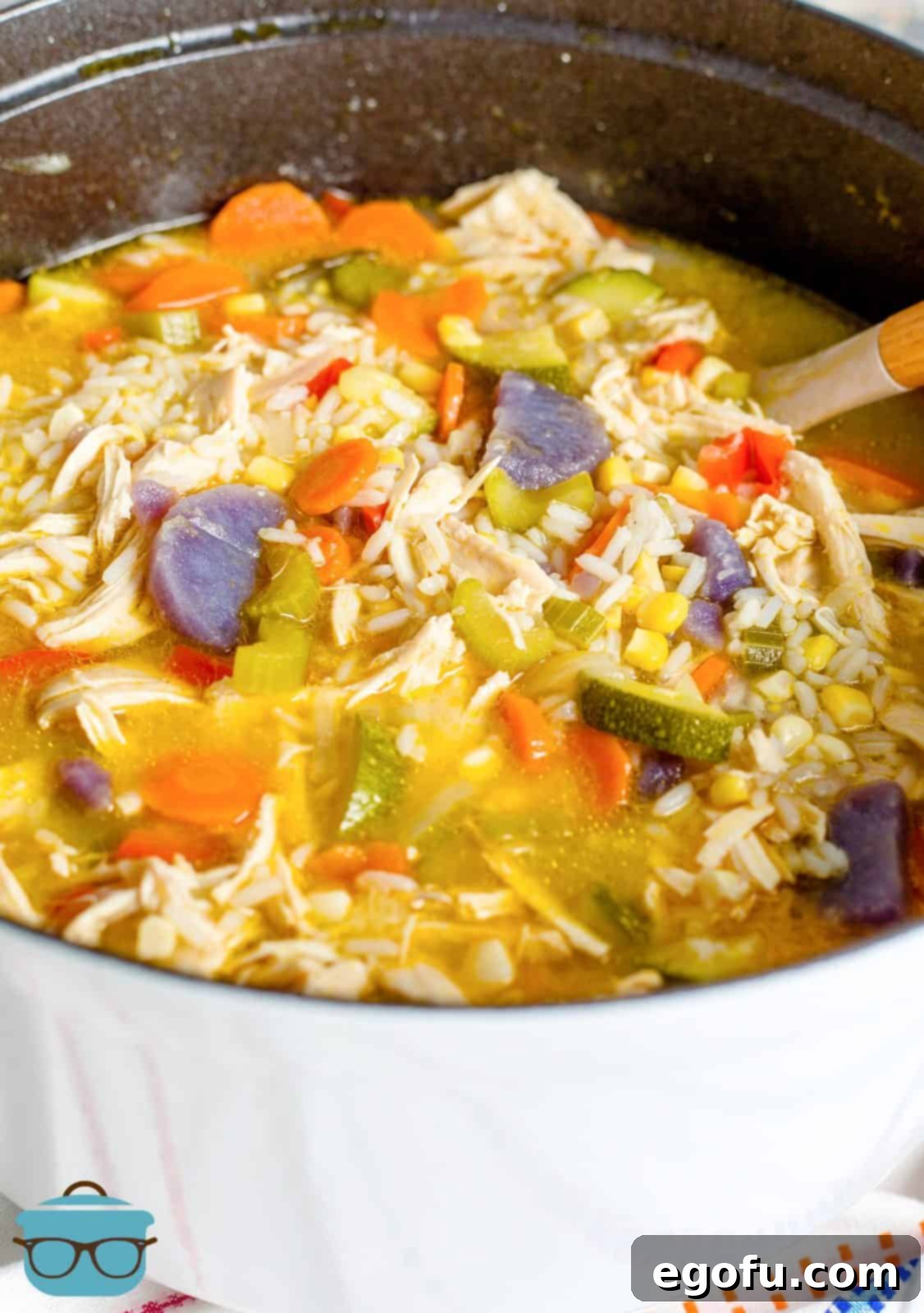 Golden Harvest Chicken and Rice Soup 2 A large pot brimming with a comforting Harvest Chicken and Rice Soup, featuring chunks of chicken, rice, and colorful vegetables, with a wooden spoon resting inside, ready to serve.