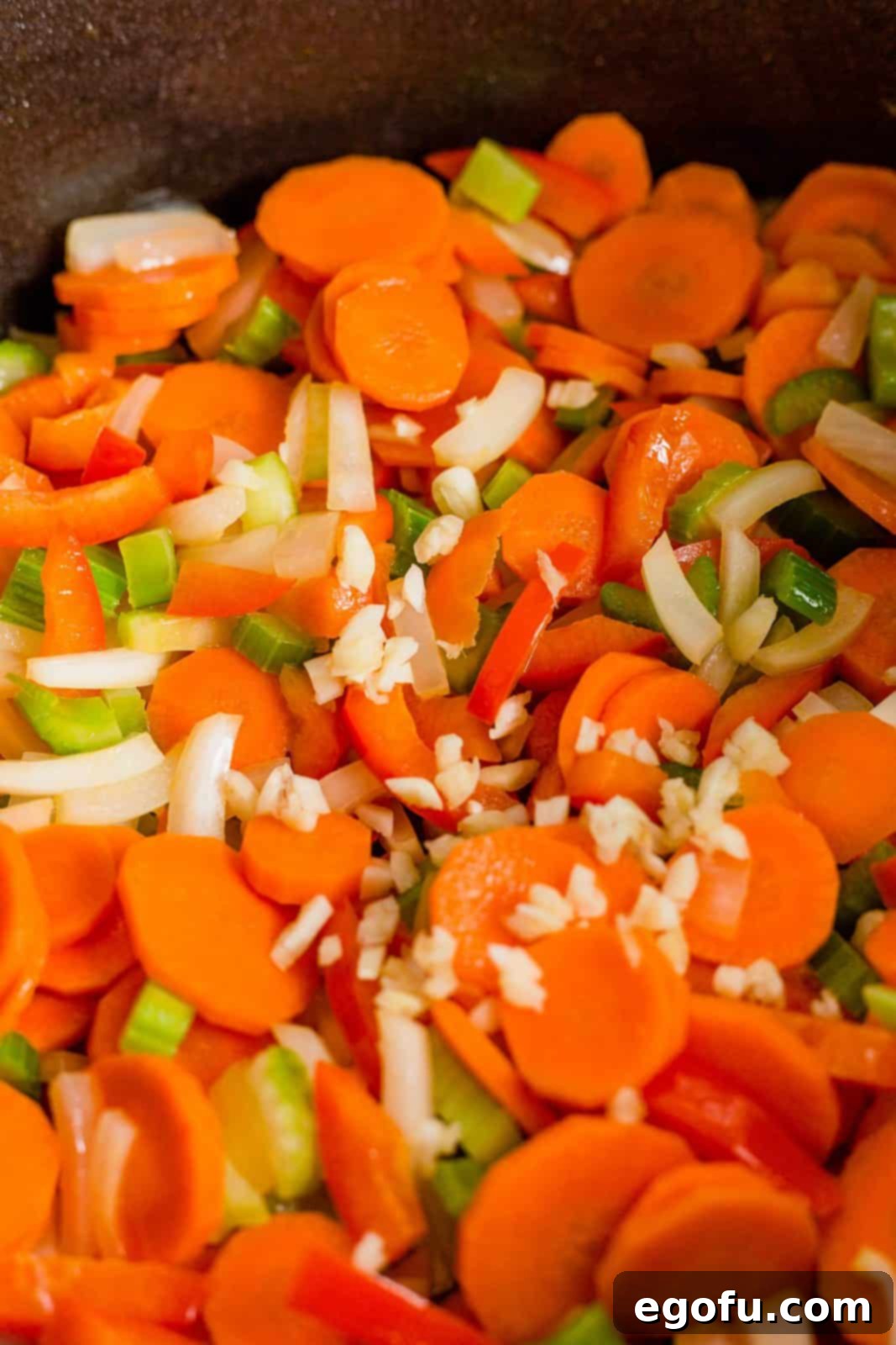 Golden Harvest Chicken and Rice Soup 5 Onion, carrots, celery, red pepper, and chopped garlic being sautéed in melted butter in a large pot, releasing fragrant aromas.