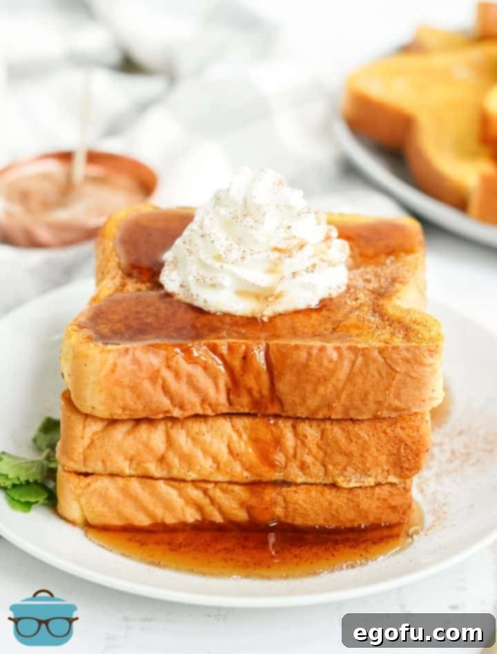 Close up of stacked Pumpkin French Toast on white plate with whipped topping and syrup.