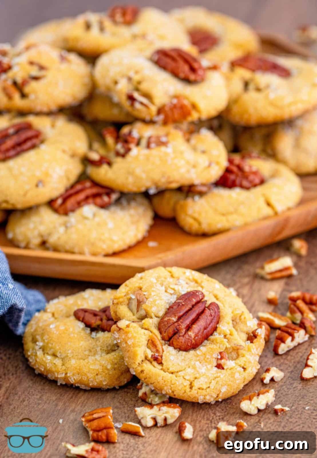 Two Butter Pecan Cookies stacked on one another with more stacked cookies on wooden board in back.