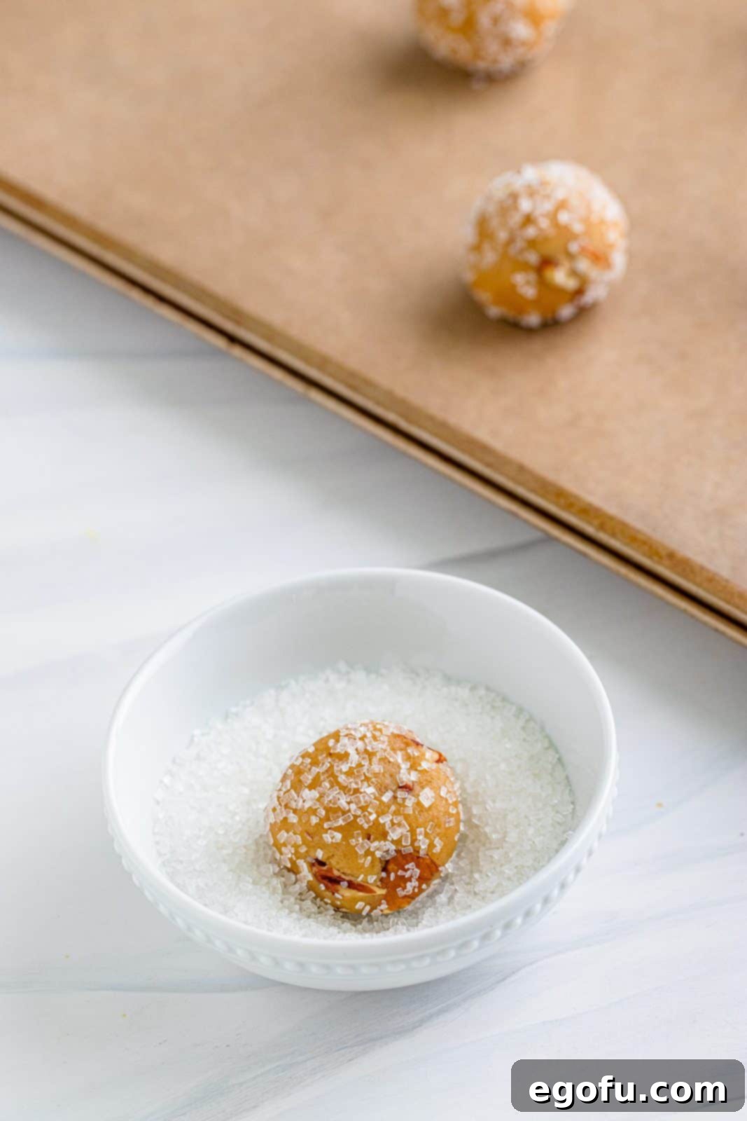 Rolled cookie dough balls being rolled into decorators sugar.