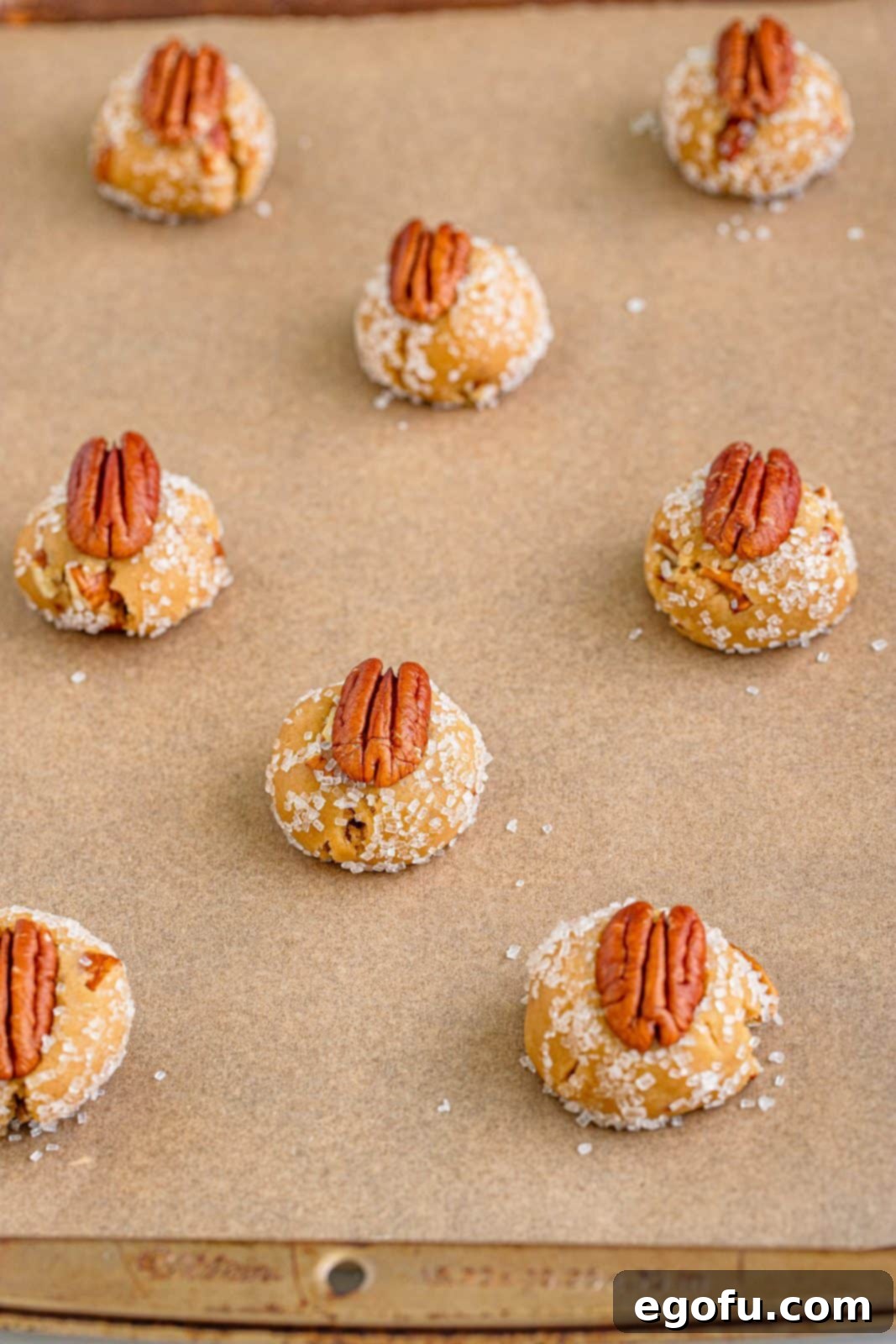 Cookie dough on lined baking sheet with pecans pressed into top of them.