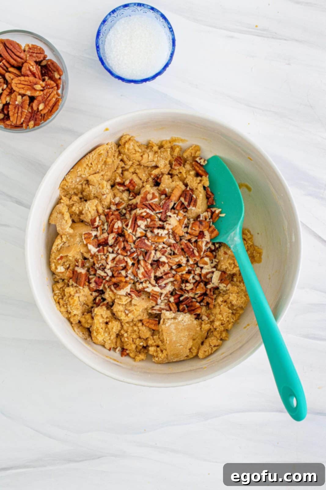 Pecans added to cookie dough in white bowl.