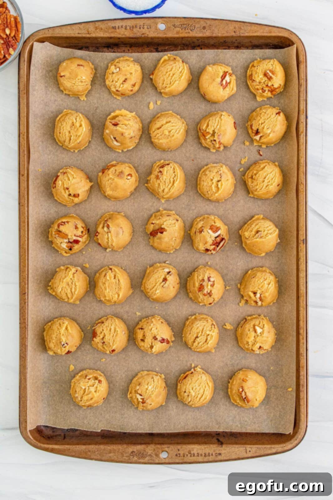 Cookie dough balls on lined baking pan ready to be cillled.