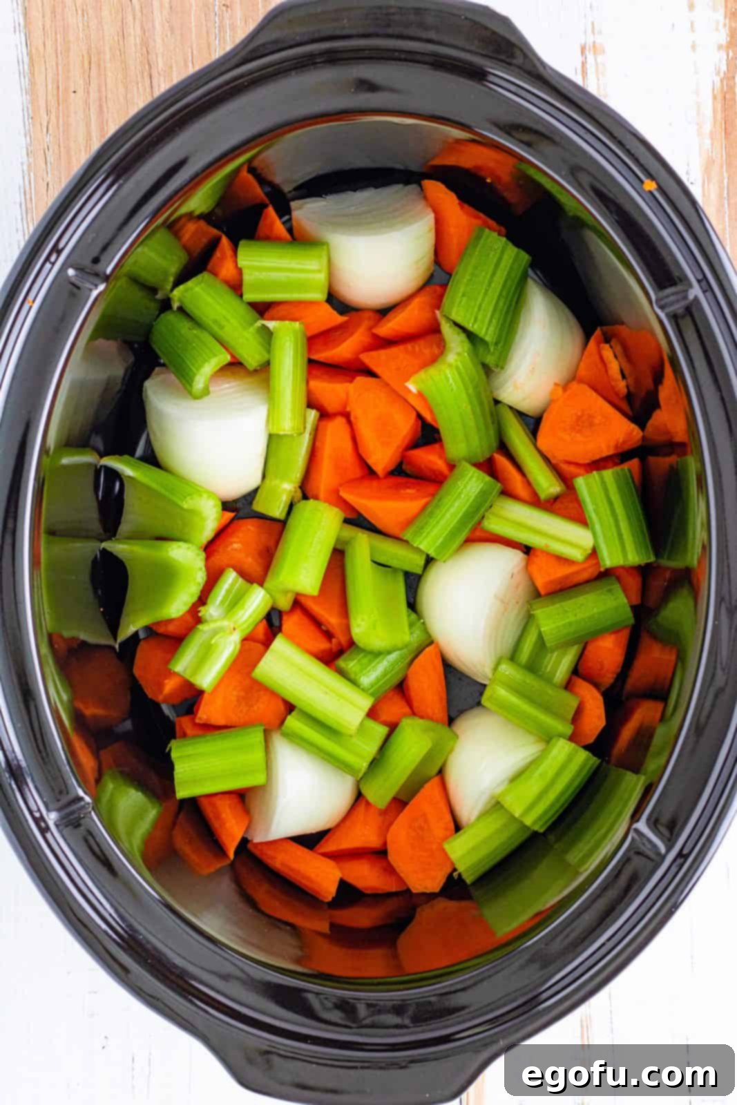 Chopped carrots, celery, and onion added to the bottom of the crock pot, creating a flavorful base.