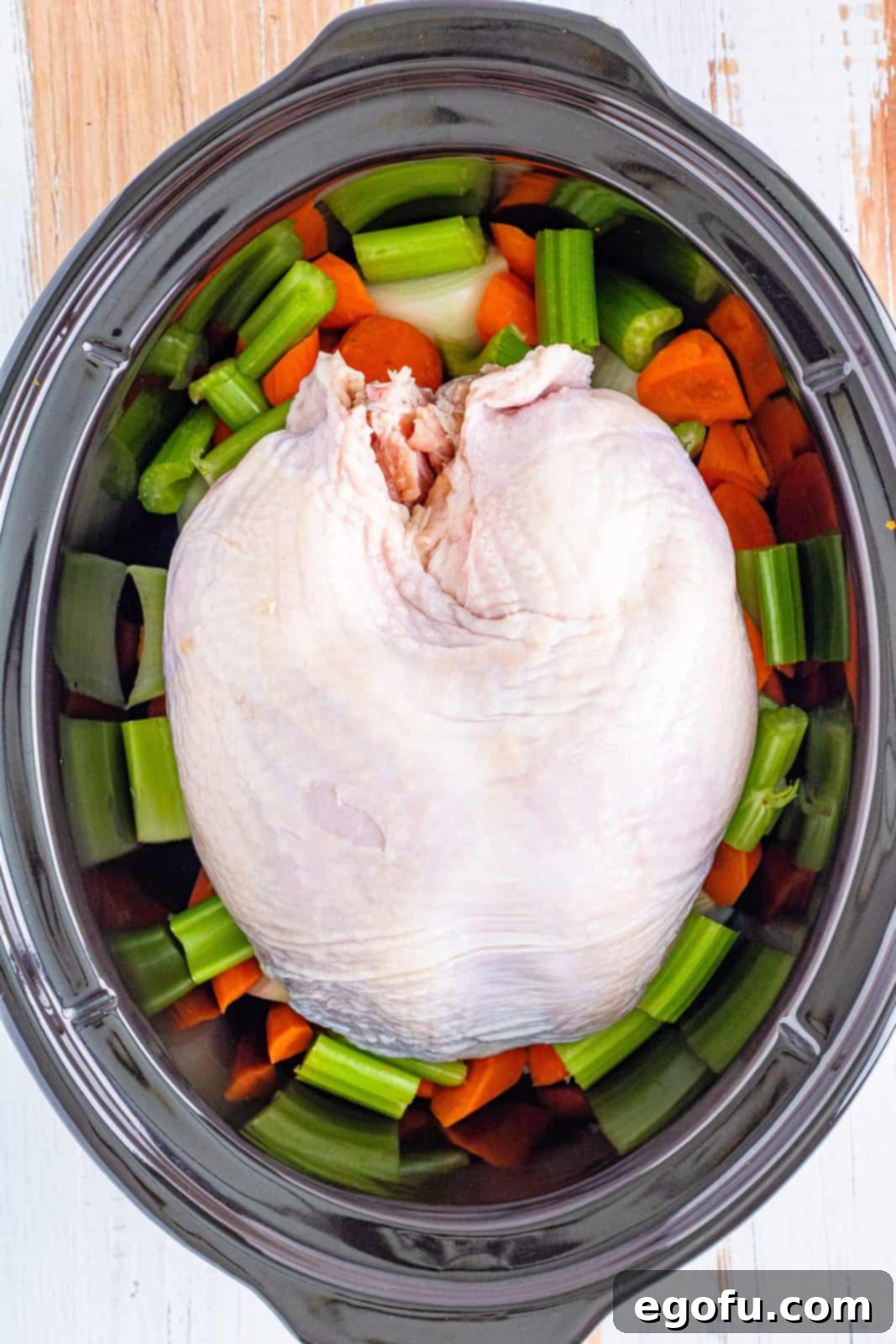 Bone-in turkey breast placed on top of the chopped vegetables in the crock pot.