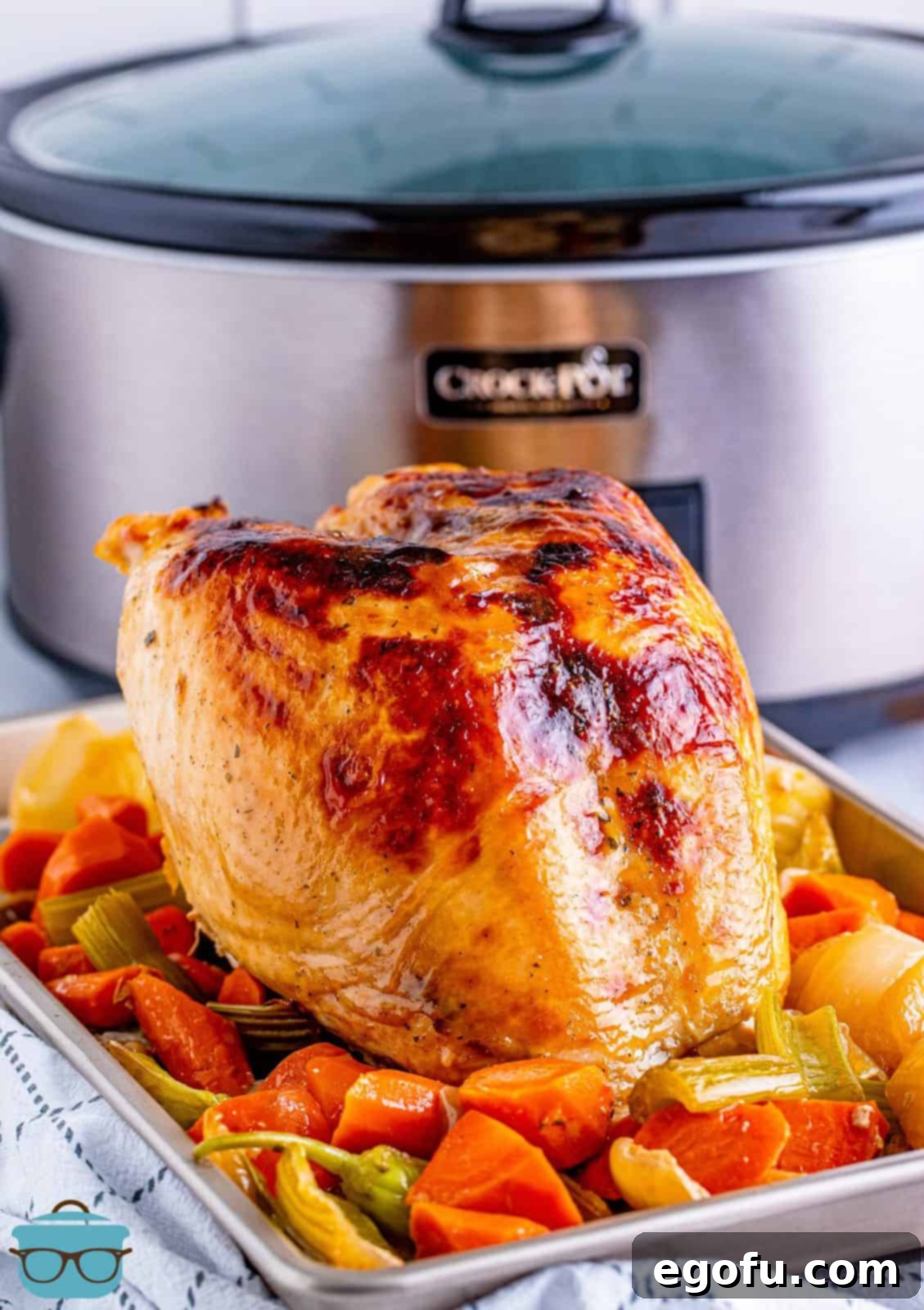 Crock Pot Mississippi Turkey Breast on a platter with vegetables, with the slow cooker in the background.