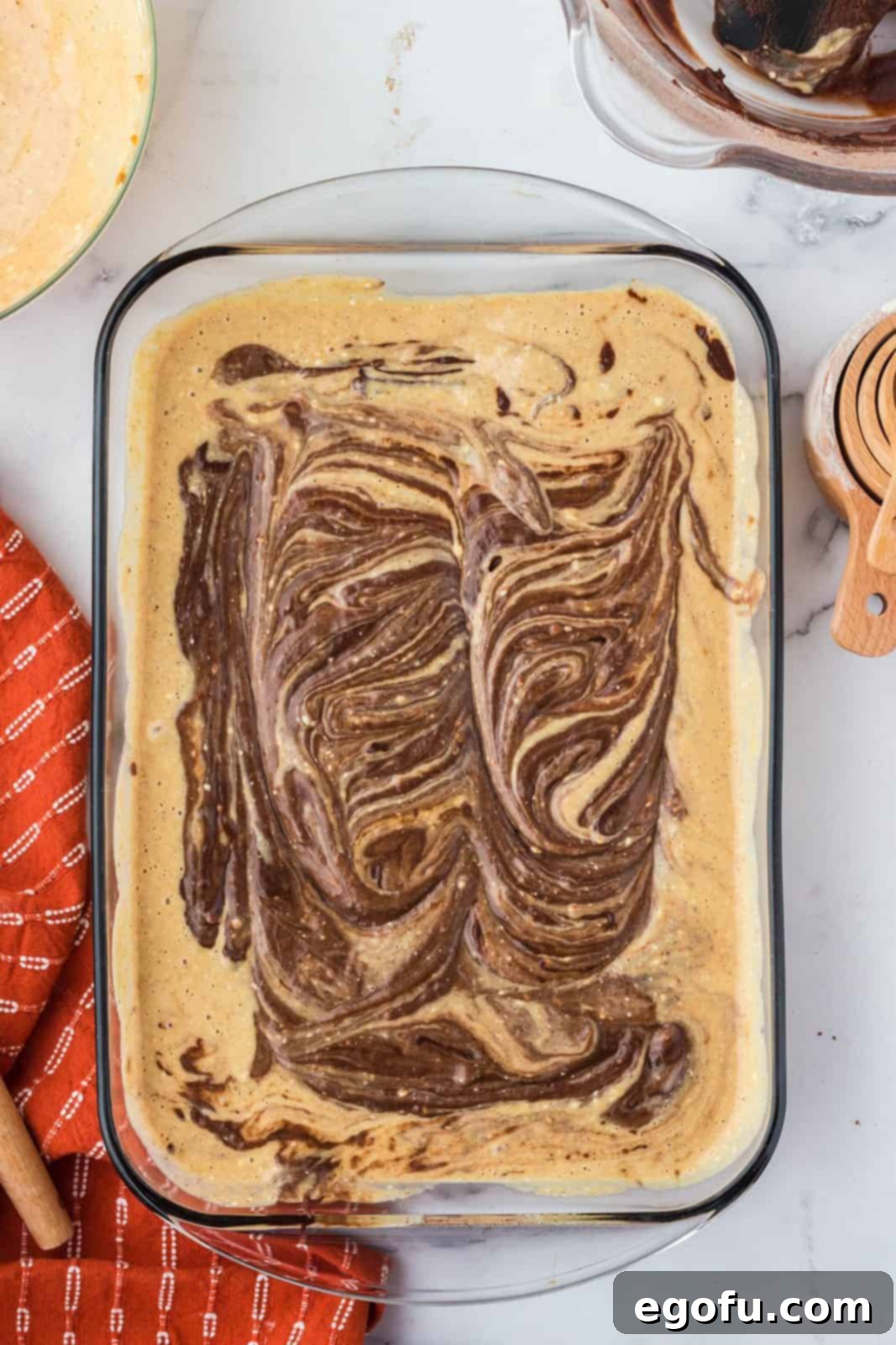 The pumpkin layer and remaining brownie batter artfully added to the pan and swirled together with a butter knife, creating a visually appealing marbled effect.