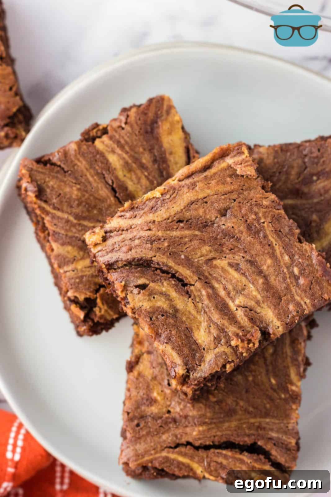 An overhead photo of perfectly cut, stacked Pumpkin Swirl Brownies arranged neatly on a white plate, showcasing their inviting texture and beautiful swirl pattern.