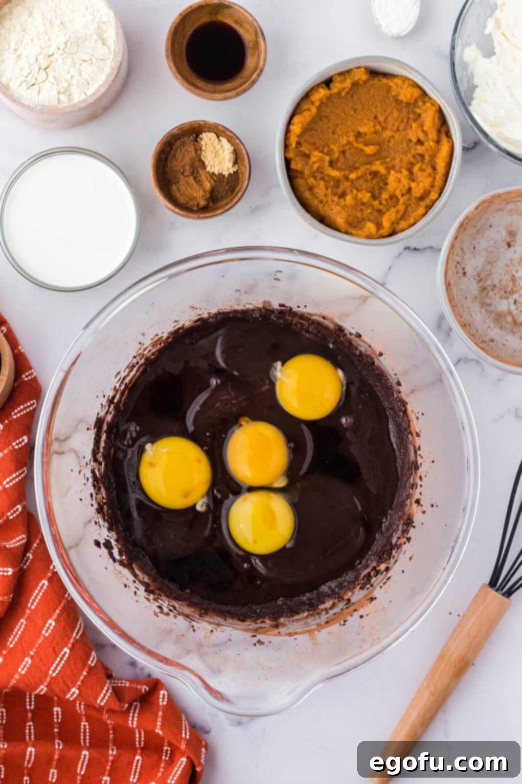 Whole eggs cracked into the cocoa and butter mixture in a bowl, ready for whisking.