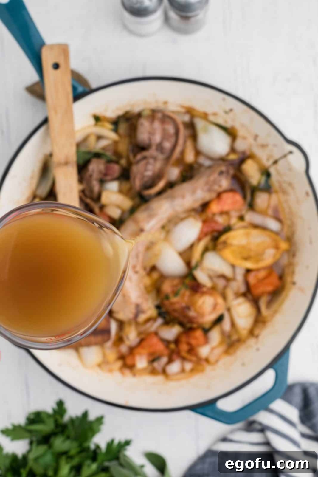 The Definitive Turkey Gravy 6 Rich turkey drippings being carefully poured over the sautéed giblets, herbs, and aromatics in a pan, initiating the simmering process for the gravy.