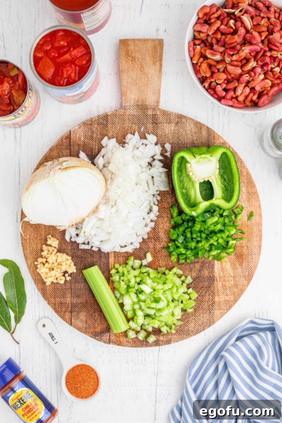Fresh vegetables, including onions, bell pepper, and celery, neatly chopped on a wooden cutting board.