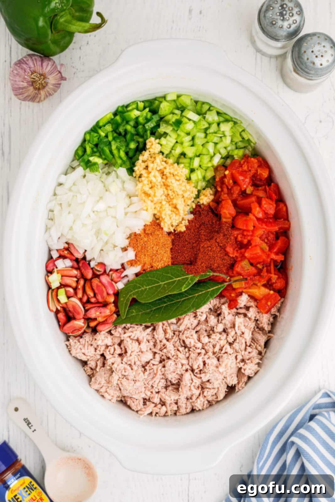 All chili ingredients, including turkey, beans, tomatoes, and vegetables, visibly combined in a large oval white crock pot, ready for slow cooking.