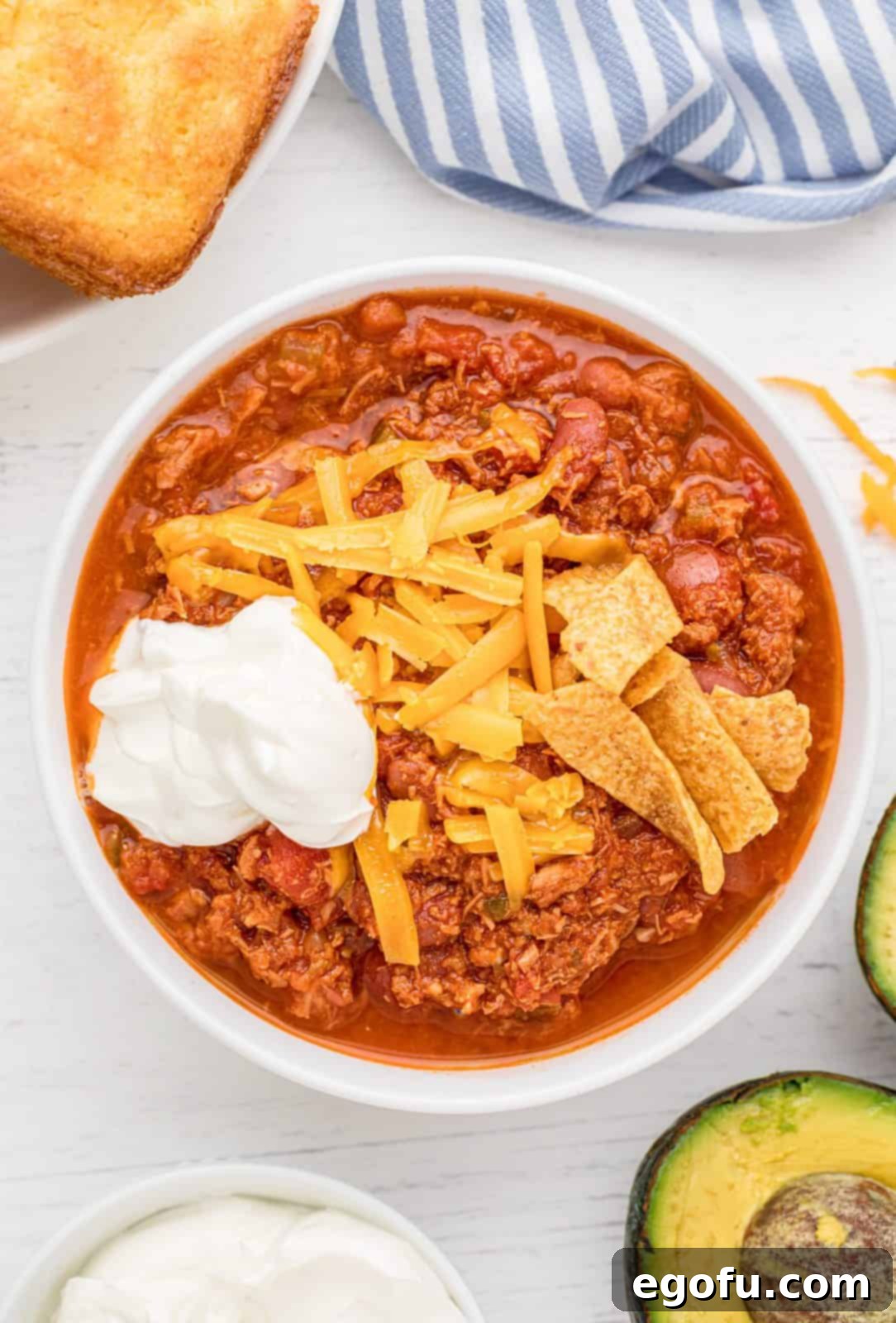 An overhead photo of a inviting bowl of Crock Pot Turkey Chili, generously topped with melted cheese, a dollop of sour cream, and a side of crispy corn chips, ready to be enjoyed.