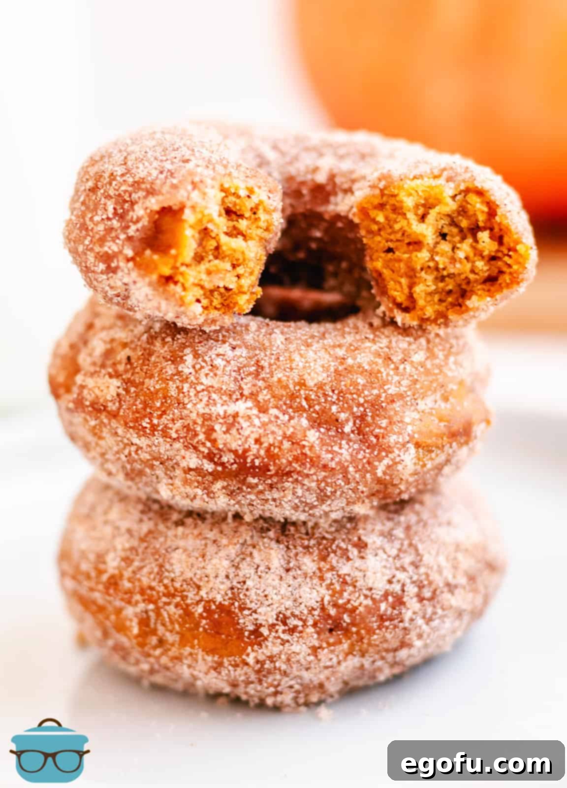 Three stacked Baked Pumpkin Donuts with top donut broken in half, revealing its soft, pumpkin-spiced interior.