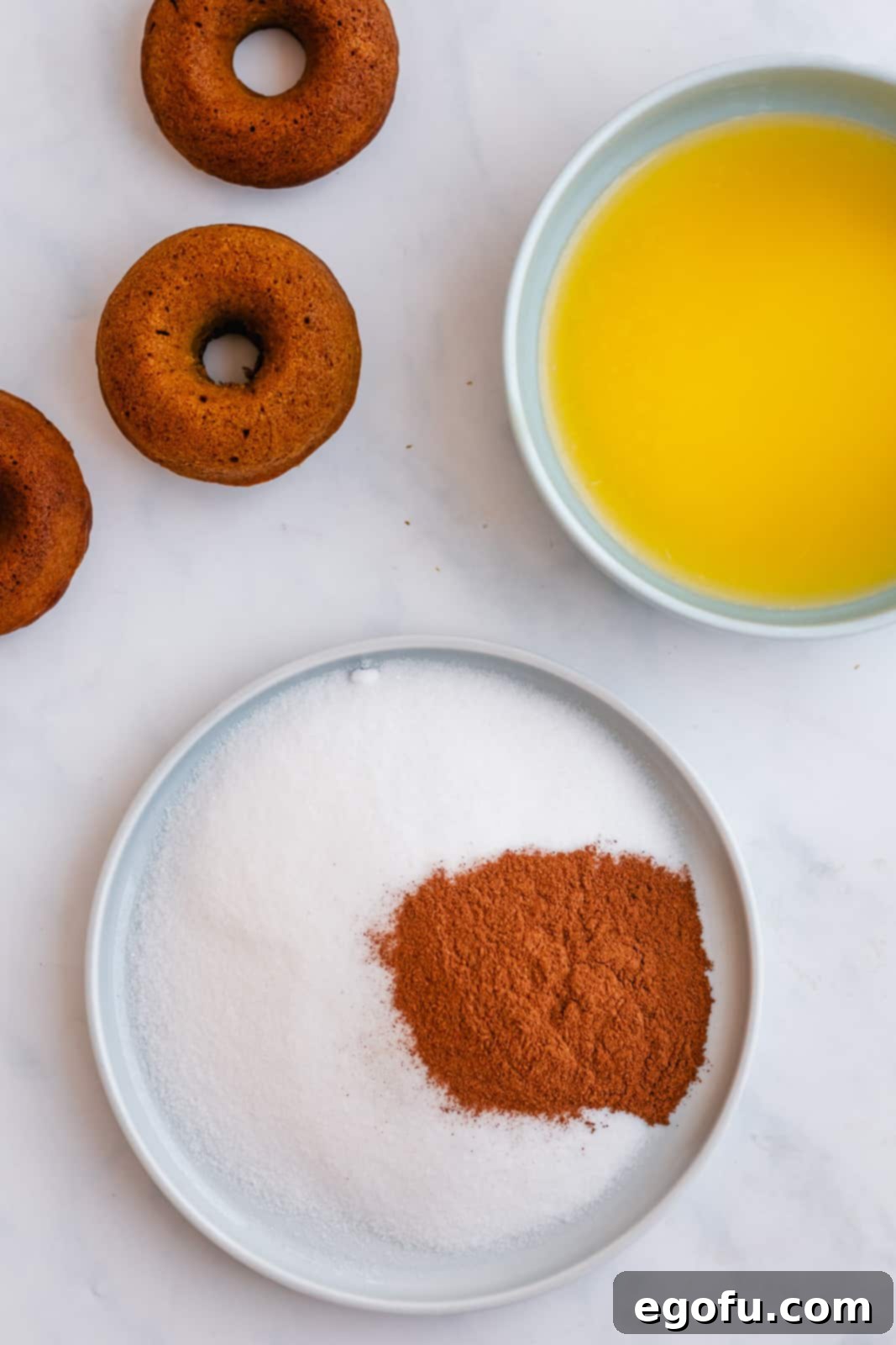 A bowl of cinnamon sugar mixture and a separate bowl of melted butter, prepared for coating the baked donuts.
