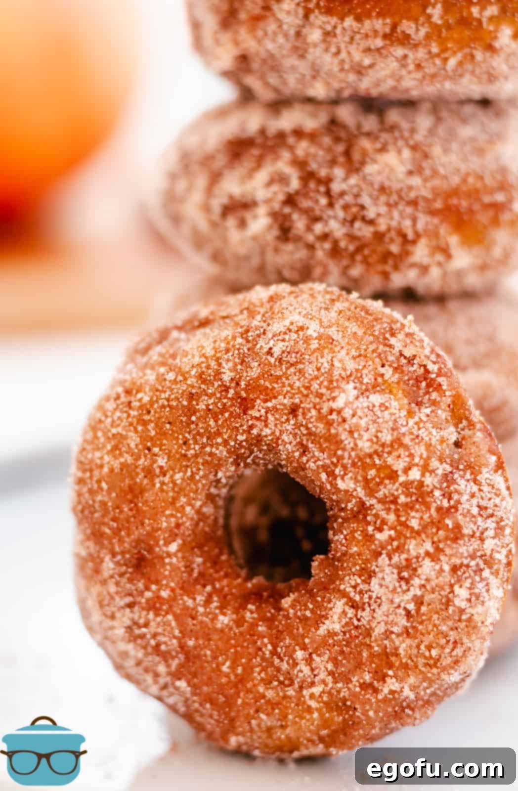 A close-up of a single Baked Pumpkin Donut, perfectly coated in cinnamon sugar, leaning against a stack of other donuts, emphasizing its inviting texture.