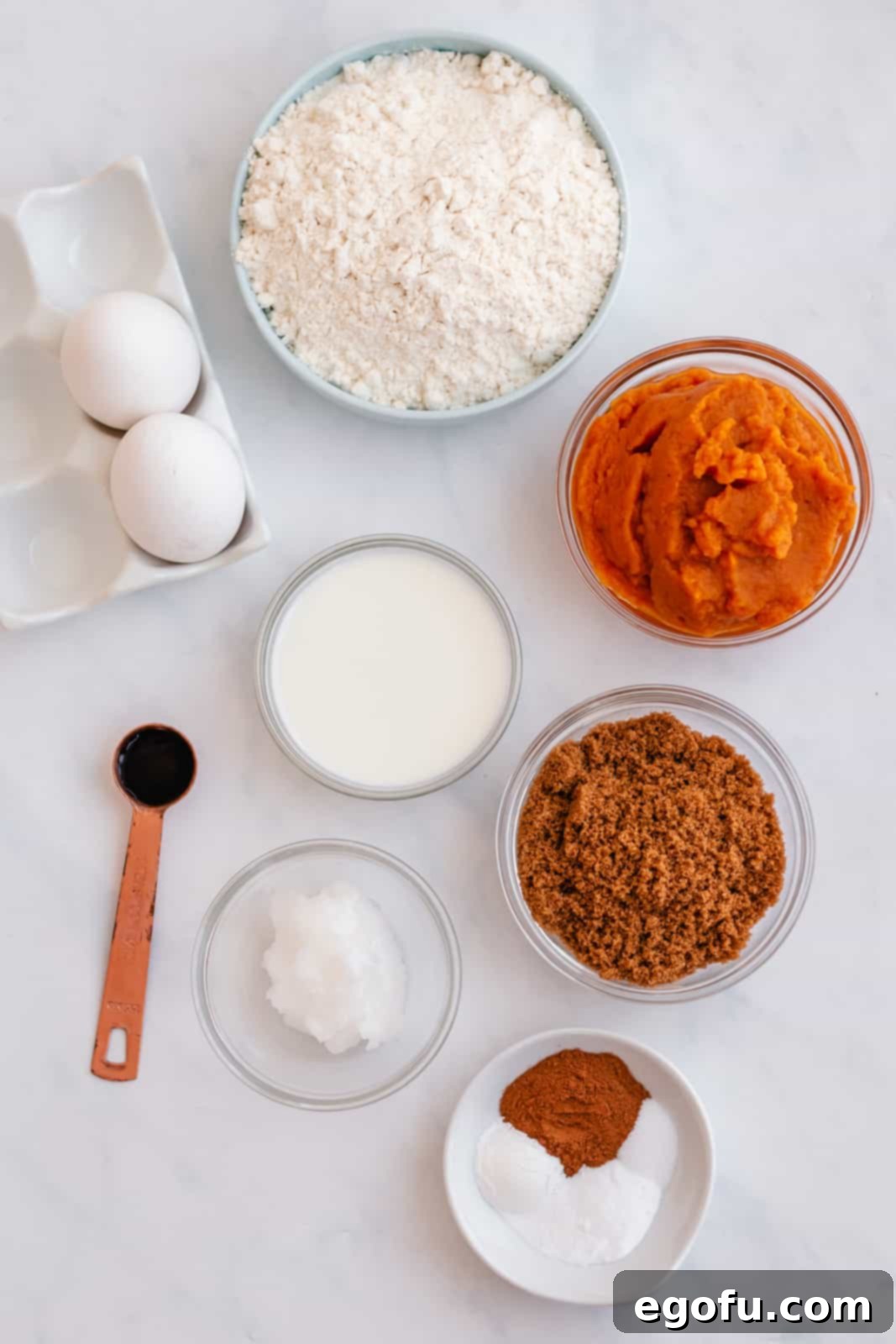 Various ingredients for Baked Pumpkin Donuts laid out on a table: all-purpose flour, baking powder, baking soda, salt, cinnamon, pumpkin pie spice, vegetable oil, brown sugar, pumpkin puree, milk, vanilla extract and unsalted butter.